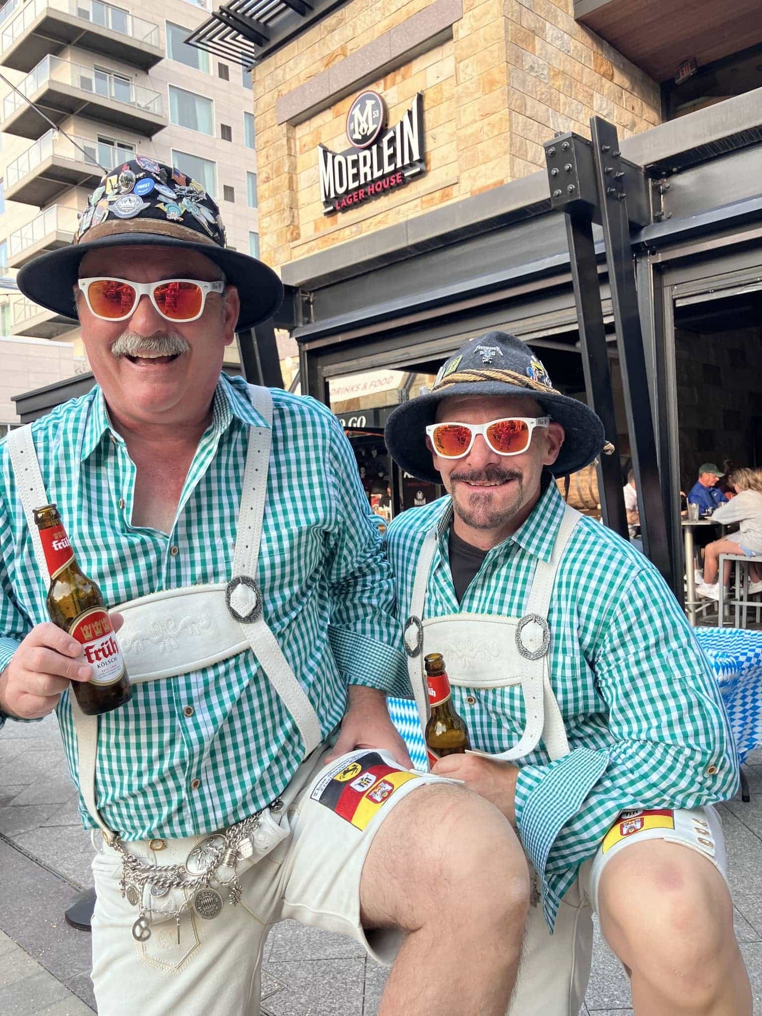 Two men in traditional Bavarian attire standing outside a building with 'Moerlein' branding.