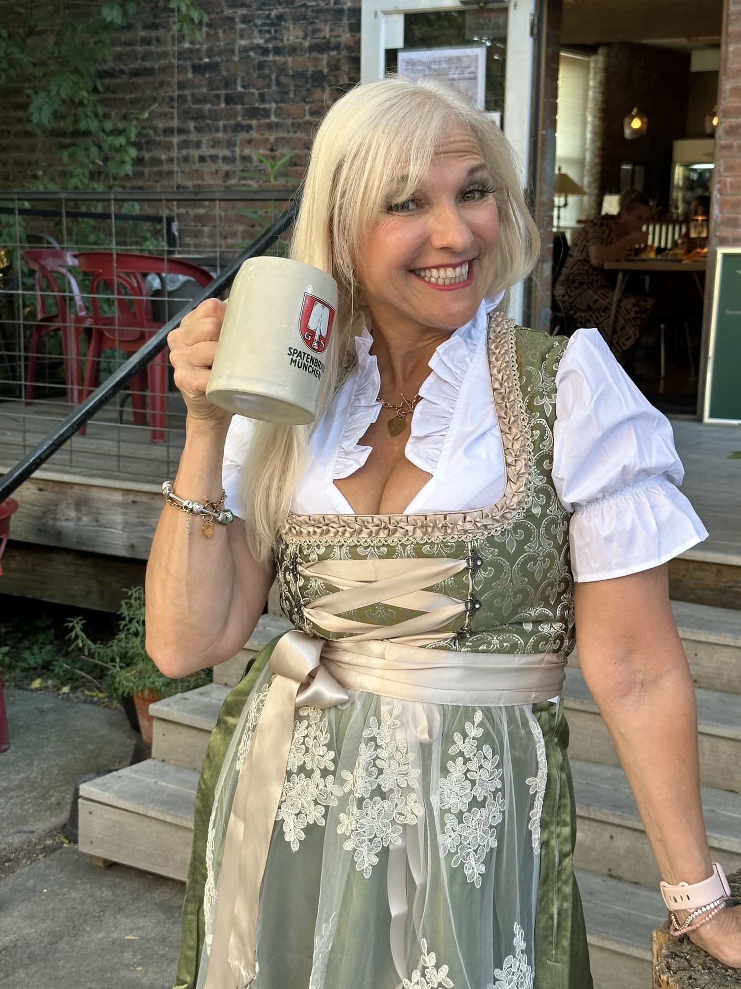 Woman in traditional German clothing holding a beer mug outdoors.