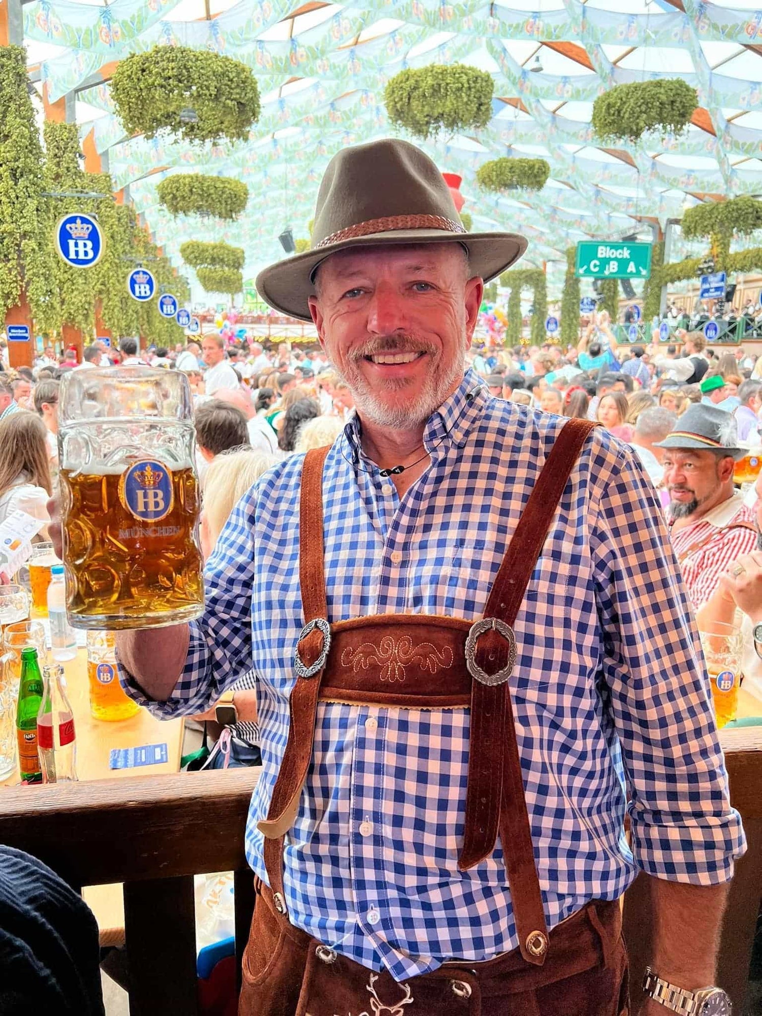 Man in traditional Bavarian attire holding a beer stein at a crowded outdoor event.