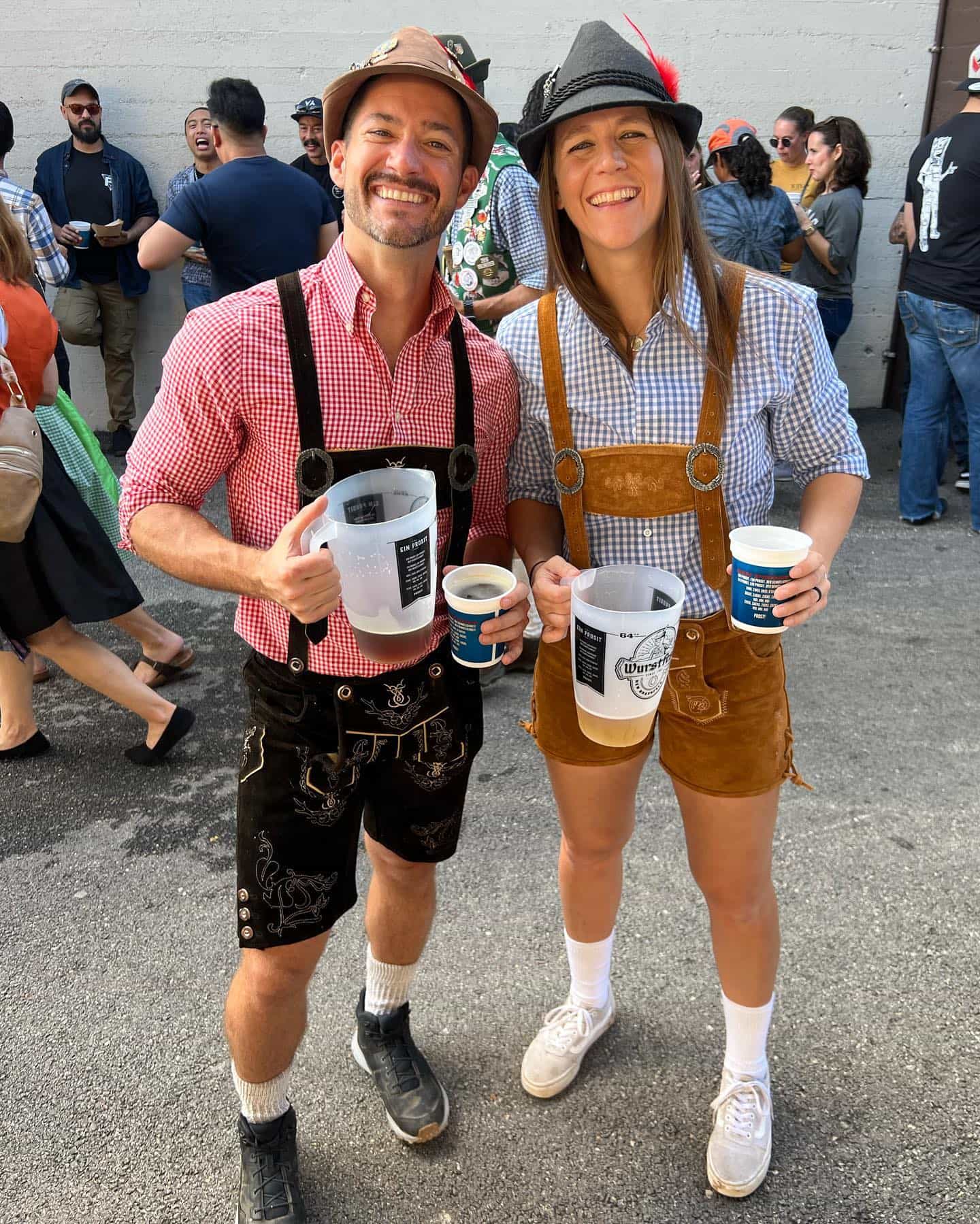 Two people in traditional Bavarian attire holding beer steins in a crowded outdoor setting.