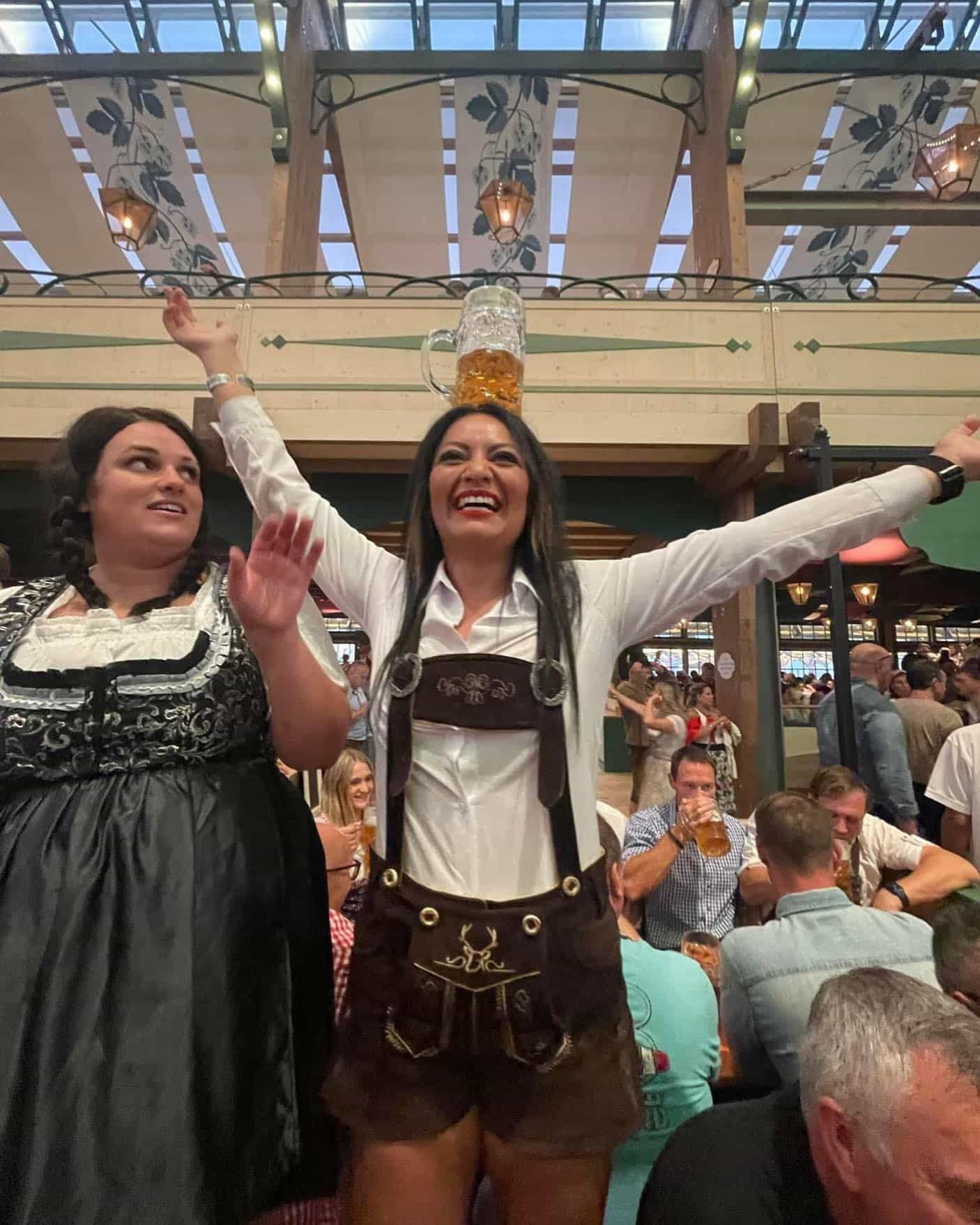 Woman in traditional Bavarian attire balancing a beer mug on her head in a festive setting.