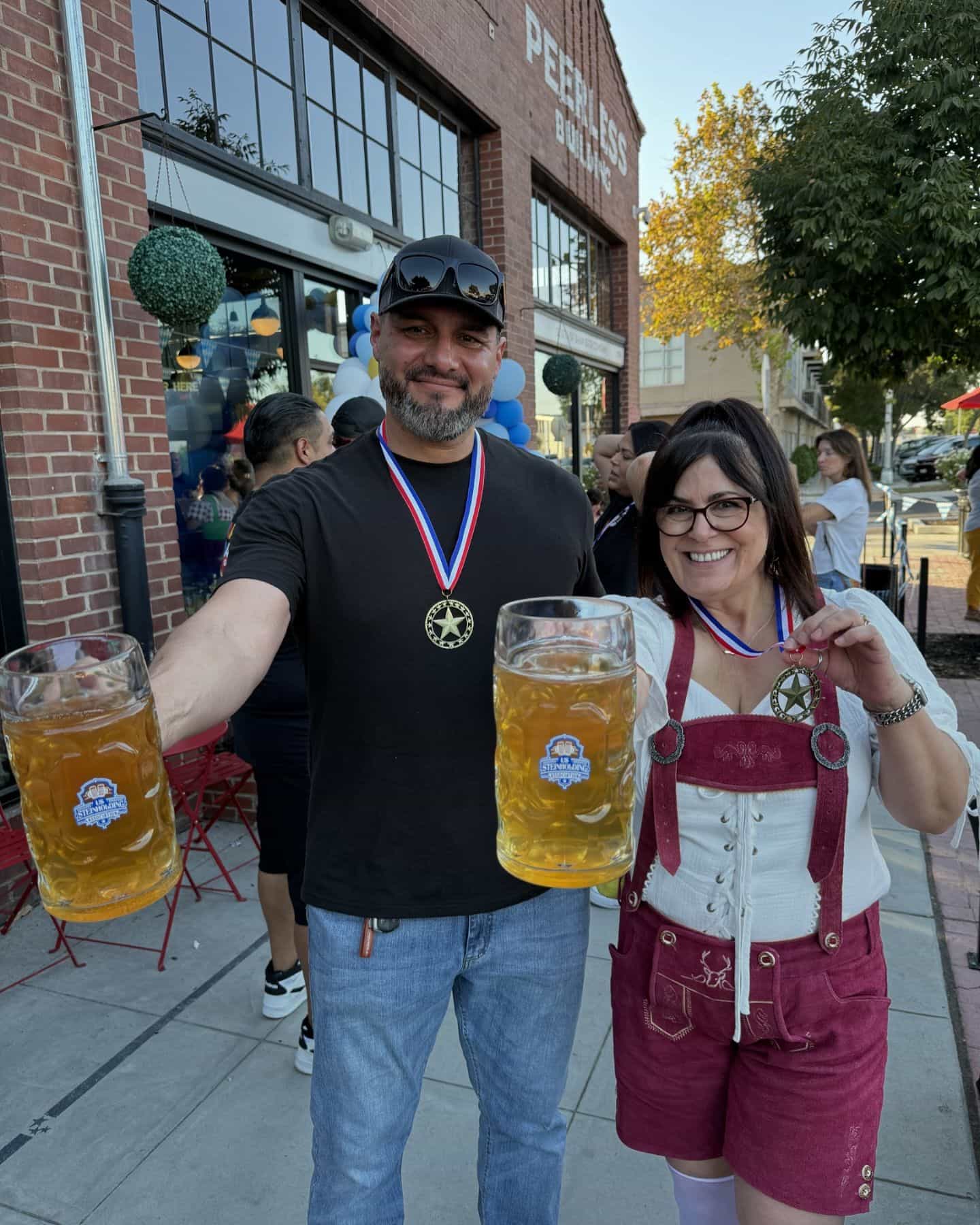 Two people holding large glasses of beer in a festive outdoor setting.