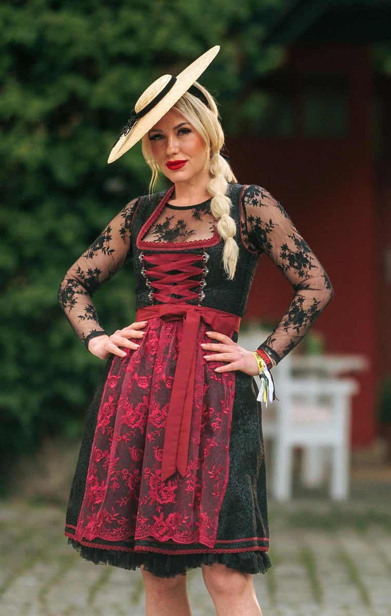 Woman wearing a traditional German dirndl with a lace top and red apron, standing outdoors.