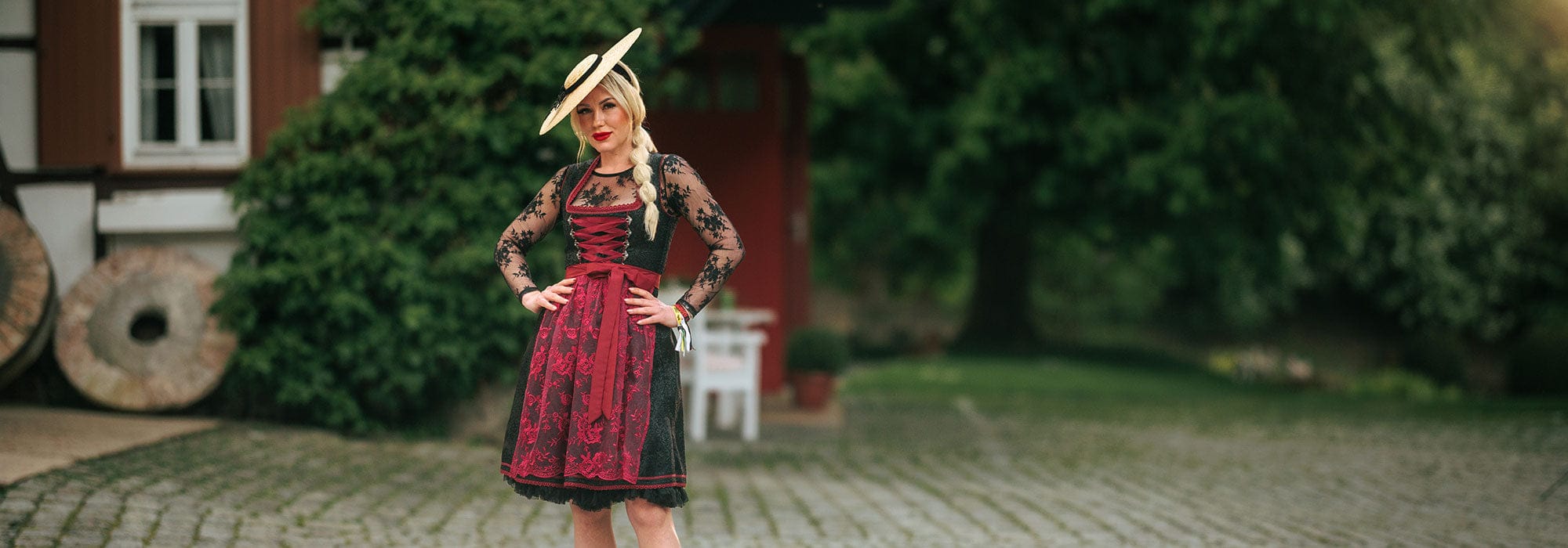Woman in traditional dress standing in front of a red building with greenery.