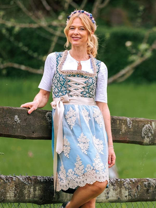 Woman in traditional Bavarian dress standing by a wooden fence with greenery in the background